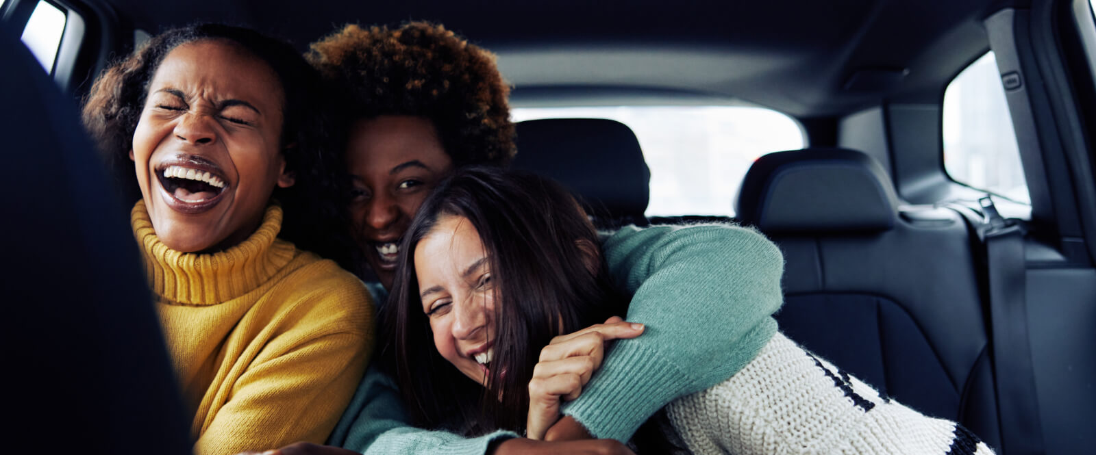 Three women in the back of a car laughing and hugging