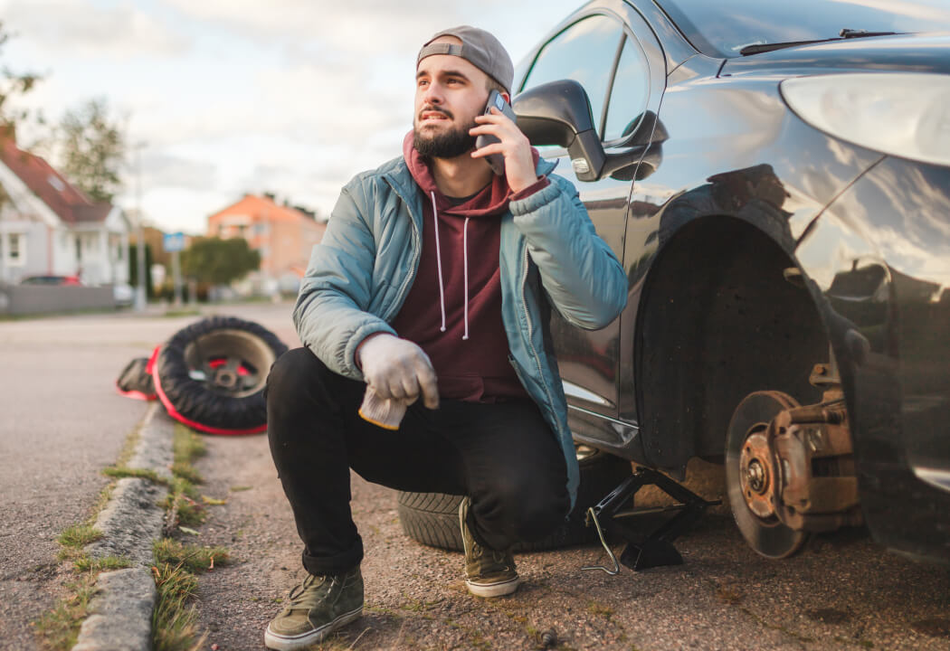 Young man squatting next to a broken down car