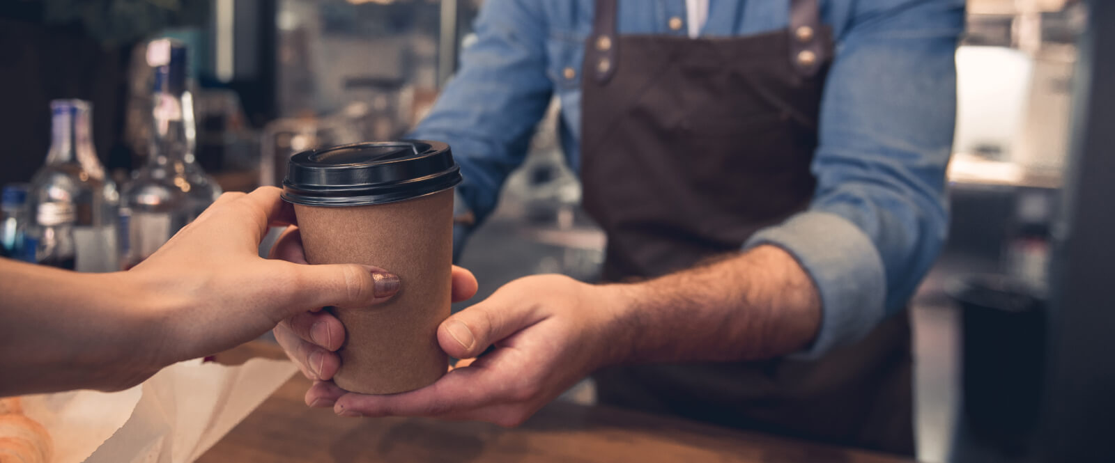 Close-up of a man's hands passing a paper coffee cup to someone