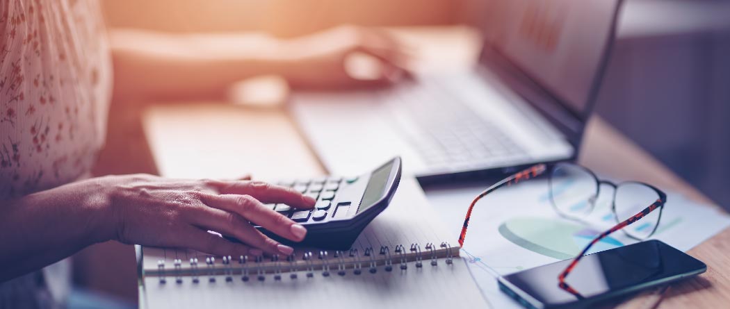 calculator, laptop, and glasses on a desk with a woman sitting behind it